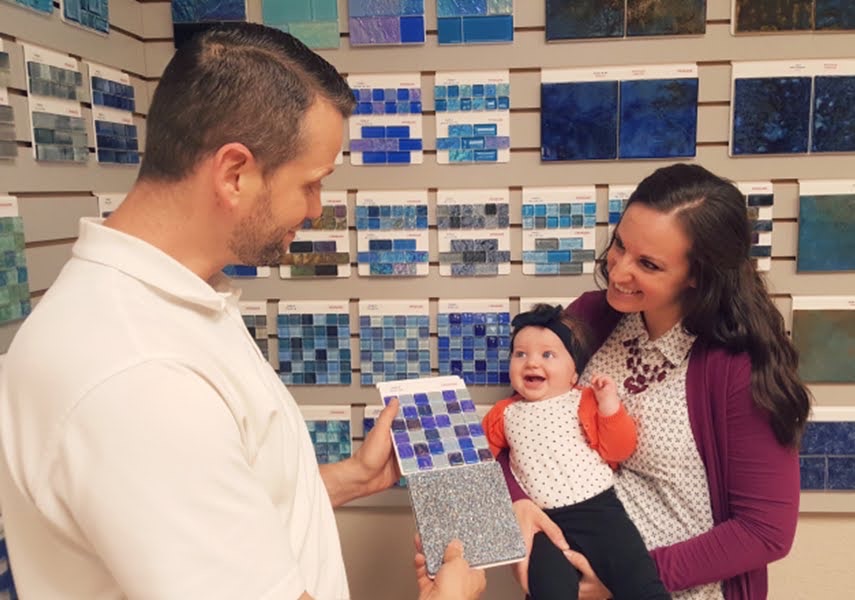 A family with a young child smiling as they look at pool tile samples in our Dallas area Swimming Pool showroom.